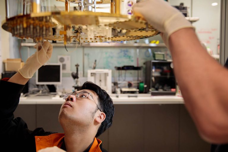 A scientist peers up at a golden disc that forms part of a quantum computing setup